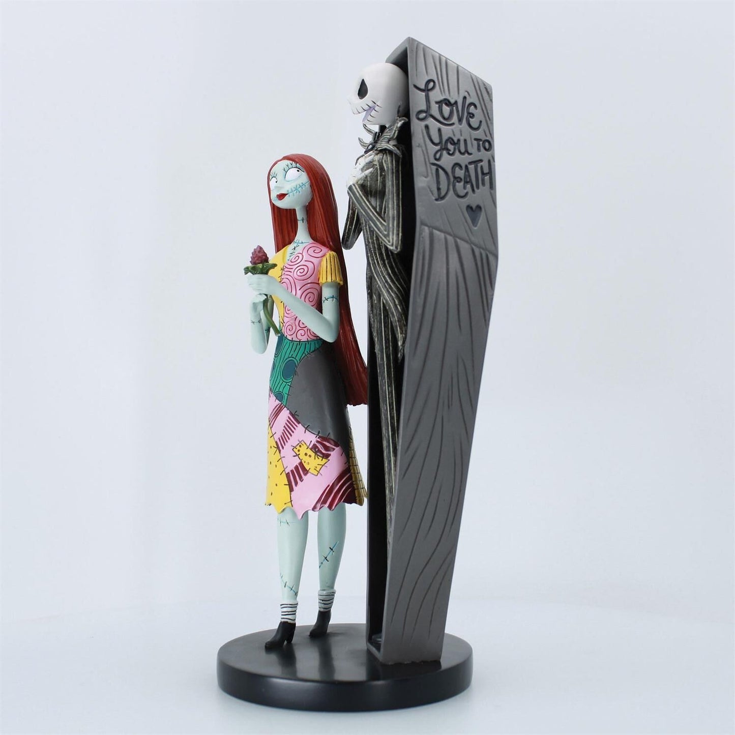 A Jack Skellington and Sally figurine from The Nightmare Before Christmas, standing on a black circular base. Sally holds a small red rose, and Jack Skellington leans against a tall gray tombstone with the words 'Love You to Death' written on it.