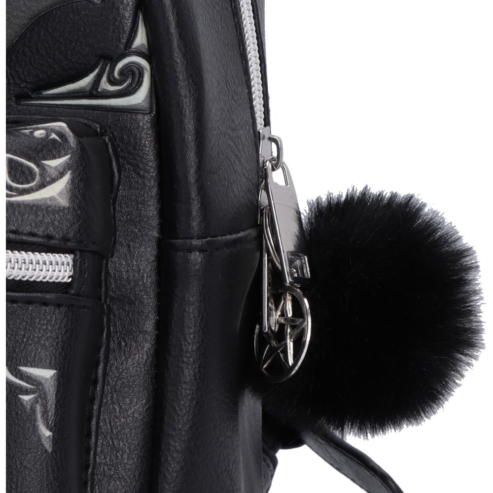 Close-up of a black faux-leather backpack featuring silver-tone hardware, a decorative silver scroll pattern on the side pocket, and a fluffy black pom-pom charm attached to the zipper pull.