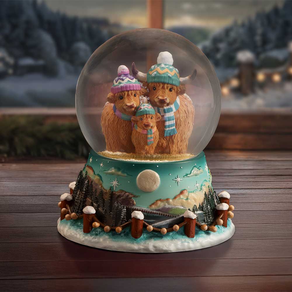 Winter Highland Cow Snow Globe showing hand-painted Highland cows wearing winter hats and scarves inside the glass globe on display