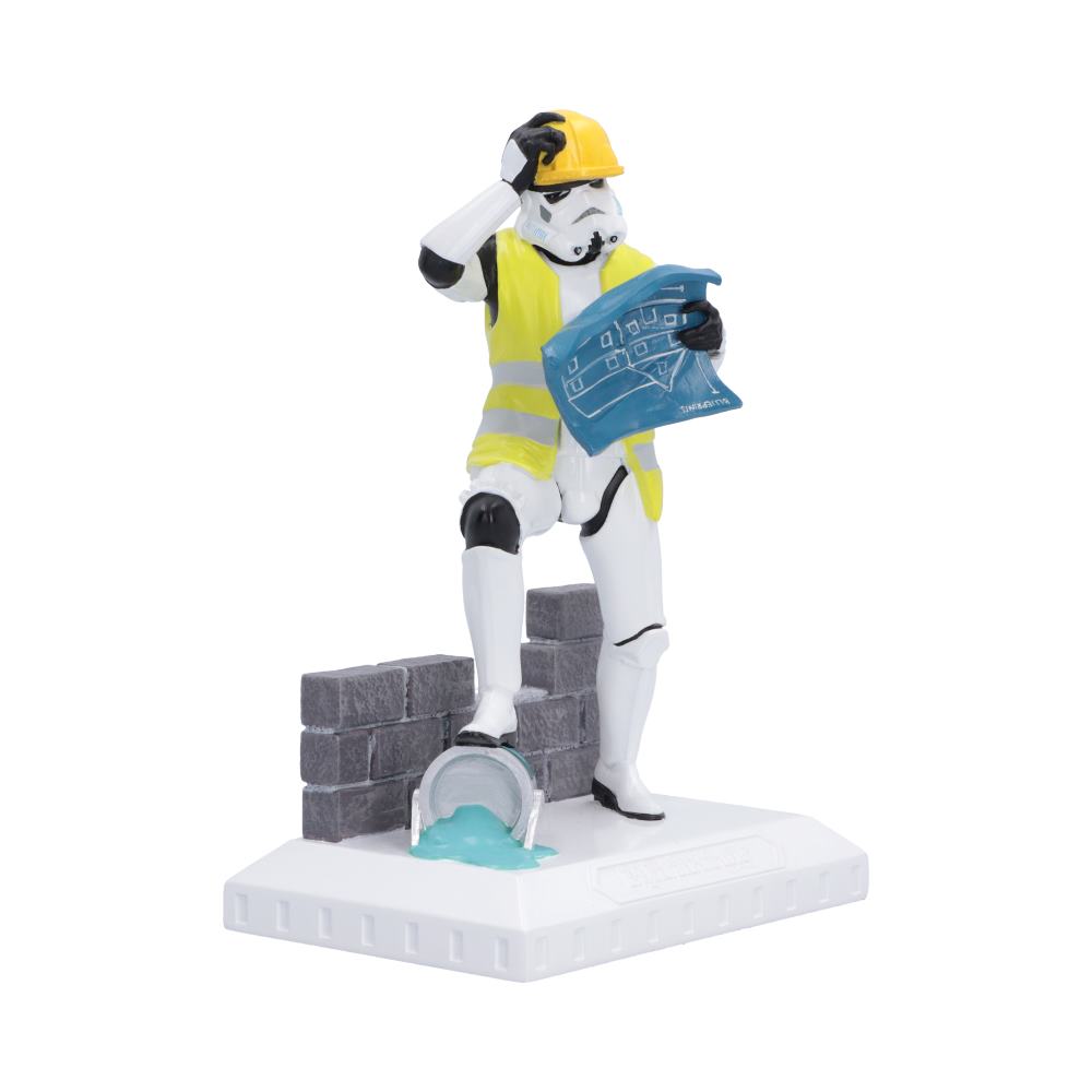A Star Wars high-quality resin collectible figurine of a Stormtrooper dressed as a construction worker, wearing a yellow hard hat and high-visibility vest while holding blue blueprint sheets, standing on a white base with a gray brick wall and a tipped-over bucket.