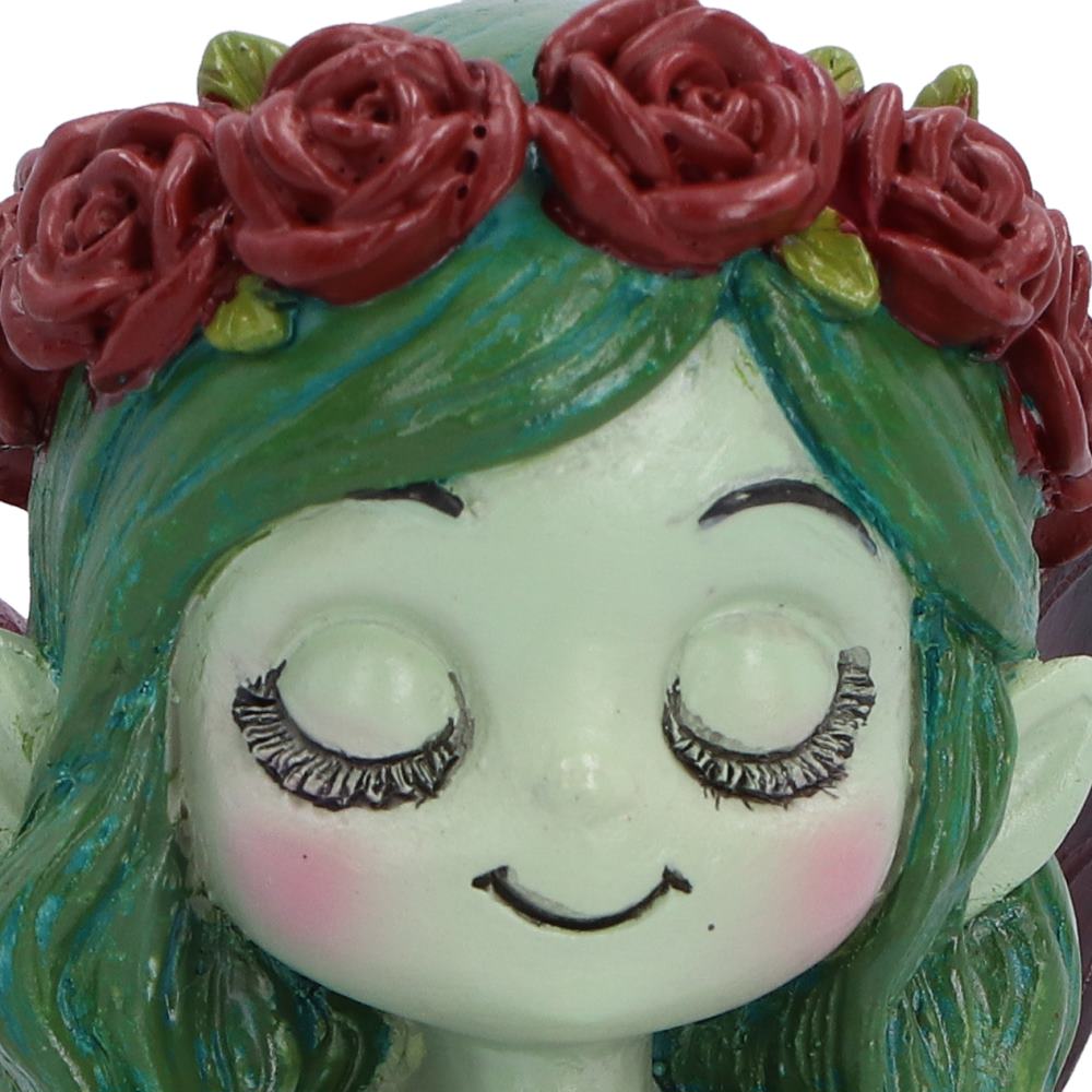 Close-up of Spirit Fairy Elaria green face with sweet smiling expression with a pale face, closed eyes, black eyelashes, pink cheeks, green hair, and a crown of dark red roses with small green leaves.